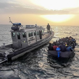 Ein überfülltes Boot voller Flüchtender schwimmt im Mittelmeer neben einem Boot der italienischen Küstenwache.