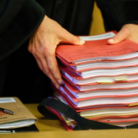 Gerichtsakten liegen in einem hohen Stapel roter Mappen auf einem Tisch.