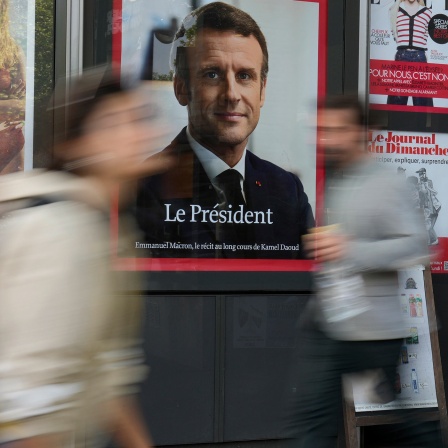 Ein Portrait des französischen Präsidenten Emmanuel Macron an einem Zeitungsstand - davor laufen Menschen (Bild: dpa)