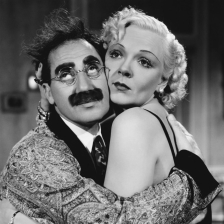 Groucho Marx und Esther Muir sitzen umschlungen auf einer Couch.