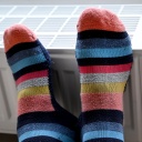 Füße in geringelten Socken liegen zum Wärmen auf einem Heizkörper in einer Wohnung.