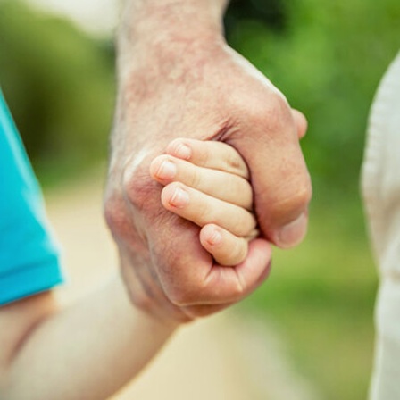 Kind hält die Hand eines älteren Menschen in der Natur.