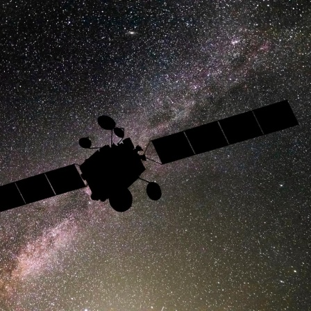 Die Silhouette eines Satelliten vorm Himmel im Weltall.