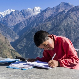 Ein Junge sitzt an einem Tisch in den Bergen und schreibt in ein Notizheft.