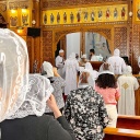 Das Bild zeigt eine koptische Messe im Kloster St.-Antonius. Mitglieder der Gemeinde stehen dabei in einem Kirchenraum mit hölzerner Vertäfelung vor einem Altar.