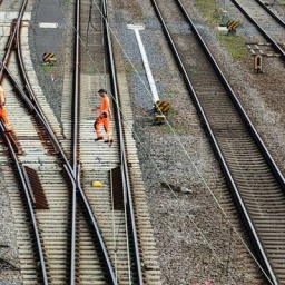 Zwei in orange gekleidete Mitarbeiter gehen über Gleise