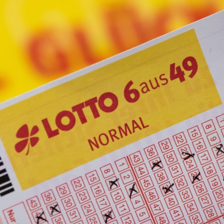 Ein Lottoschein mit der Aufschrift "Lotto 6 aus 49" ist vor einem Schriftzug "Viel Glück" zu sehen.