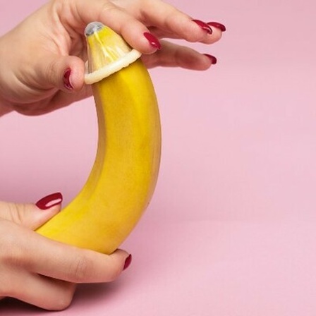 Eine Hand streift ein Kondom über eine Banane.