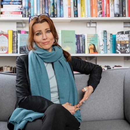 Die Schriftstellerin Elif Shafak sitzt auf einem grauen Sofa. Im Hintergrund ist ein Bücherregal zu sehen.