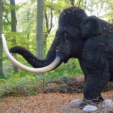 Eine Mammut-Nachbildung steht in einem Wald.