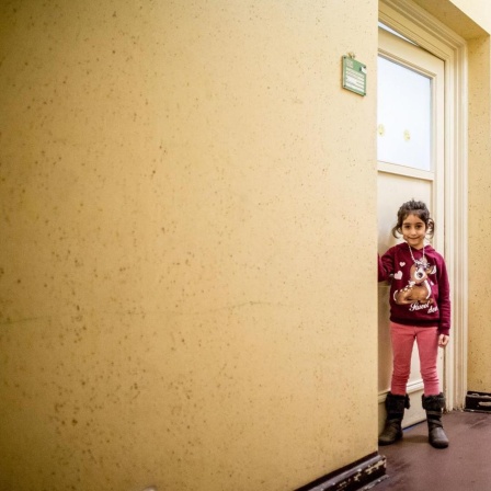 Farbfoto von zwei Personen, die in einem Hausflur stehen und in die Kamera lächeln. Es sind ein kleines ca. siebenjähriges Mädchen und ihr erwachsener Bruder, Flüchtlinge aus Syrien.