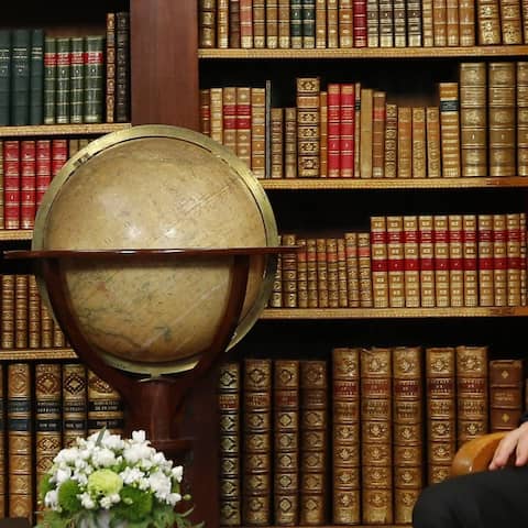 Russlands PräsidentPutin sitzt in vor einer russischen Fahen und lacht