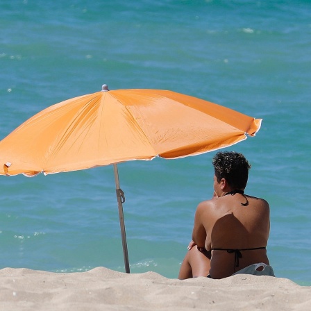 Frau sitzt am Strand unter einem Sonnenschirm