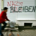 Eine Geschäftsfront ist mit dem roten Schriftzug "NAZIS RAUS", besprüht. Darüber hat jemand in Schwarz "BLEIBEN" geschrieben.