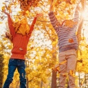 Kinder spielen im Herbstlaub, das von Bäumen fällt.
