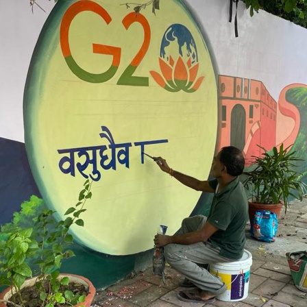 G20 Gipfel in Neu Delhi, ein Mann malt das G20-Logo mit Lotusblüte auf eine weiße Mauer