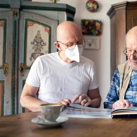 Ein Mann schaut mit einem Pflegebedürftigem in dessen Haus ein Fotobuch an 