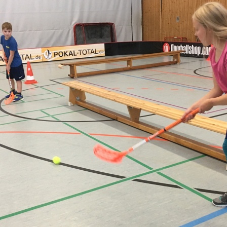 Zwei Kinder passen sich einen Ball beim Floorballspiel zu.