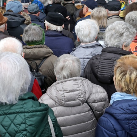 Eine Große Gruppe alter Menschen in Winterjacken steht an, um Einlass in eine Veranstaltungshalle zu bekommen.