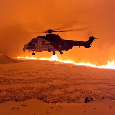 Ein Hubschrauber fliegt in der Nähe von Magma, das auf einem Hügel in der Nähe von Grindavik auf der isländischen Halbinsel Reykjanes fließt.