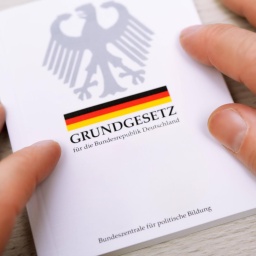 Zwei Hände streichen über die Ränder eines deutschen Grundgesetzes.