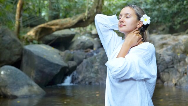 Eine Frau steht im Wald vor einer Quelle.