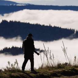 Ein Mann steht mit einer Fotokamera auf einem Berg und schaut in die Ferne – in Schwarzwald-Landschaft mit Nebel in den Tälern.