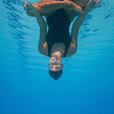 Eine Frau kopfüber unter Wasser in Meditationshaltung.