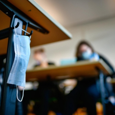 Mundschutzmaske hängt an einem Schülertisch während des Präsenzunterrichts.