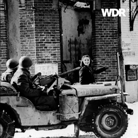 Eine junge Frau zeigt in einem Jeep sitzenden amerikanischer Soldaten eine Wegrichtung. Fotoaufnahme aus dem Jahr 1945.