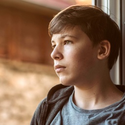 Junge schaut traurig und nachdenklich aus dem Fenster