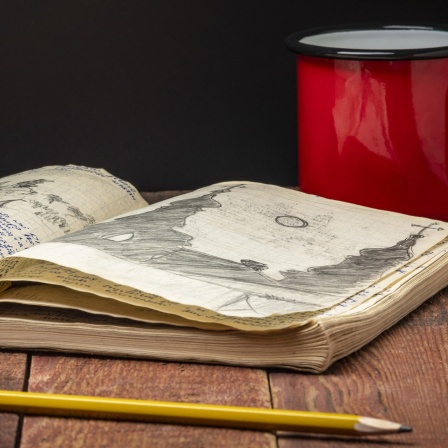 Vintage-Expeditionsjournal auf einem rustikalen Picknicktisch mit einer Tasse Tee.