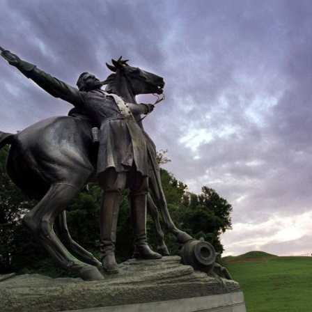 Untersichtige Aufnahme des Standbild eines Mannes zu Pferde vor düster Wolken-verhangenem Himmel.
