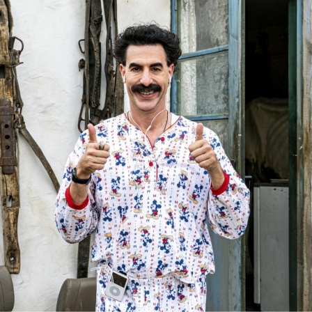 Szene aus dem neuen Borat-Film: Sacha Baron Cohen trägt einen Micky-Maus-Pyjama und blickt grinsend in die Kamera, beide Hände zeigen ein "Daumen hoch" 