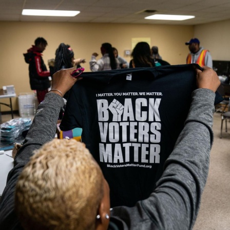 Eine Frau hält ein T-Shirt mit der Aufschrift "Black Voters Matter" in die Höhe.