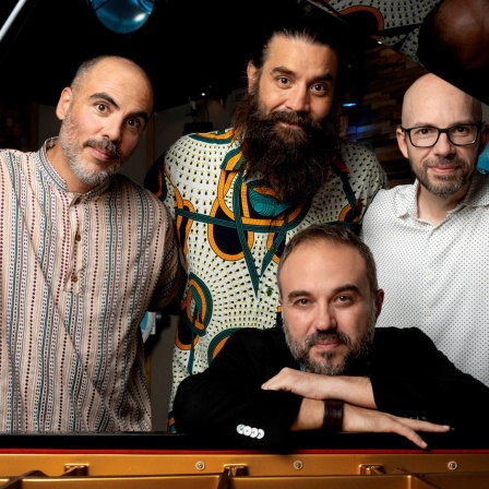 Vier männliche Musiker hinter einem Flügel schauen in die Kamera - Das Moisés P. Sanchez Quartett