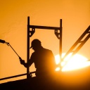 Ein Bauarbeiter steht mit einem Gasbrenner beim Bau eines Mehrfamilienhauses im Neubaugebiet Kronsrode, als am Horizont die Sonne aufgeht.