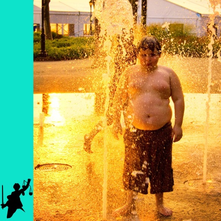 Ein junges Mädchen und ein Junge spielen mit Wasserfontänen im Battery Park in New York City bei Sonnenuntergang.