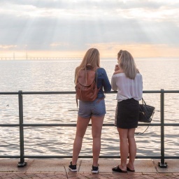 Zwei junge Frauen von hinten an einem Seeufer.