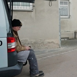 Ein Mann sitzt bei geöffneter Heckklappe auf der Ladefläche eines Autos.
