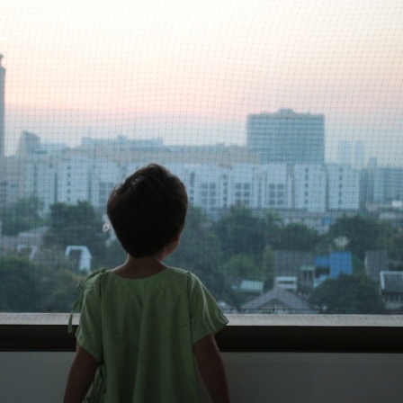 Ein Kind schaut aus einem Fenster auf Hochhäuser.