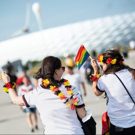 Zwei weibliche Fußballfans kommen mit Regenbogenfahnen zum Stadion in München.