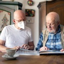 Ein Mann schaut mit einem Pflegebedürftigem in dessen Haus ein Fotobuch an 