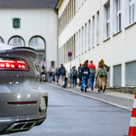 Pylonen und ein Auto stehen auf der Straße vor einer Schule