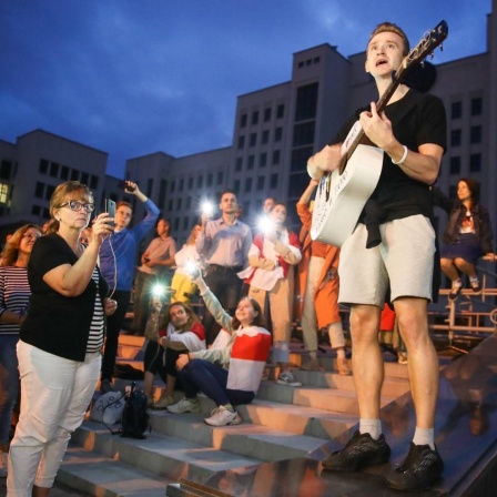 Ein junger Gitarrist gibt in Minsk abends auf einen Platz ein spontanes Konzert. Das Publikum macht Fotos, einige haben sich in die belarusische Fahne gewickelt. Valery Sharifulin/TASS PUBLICATIONxINxGERxAUTxONLY TS0E4073