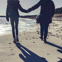 Silhouette von zwei Frauen, die Hand in Hand am Strand spazieren gehen.