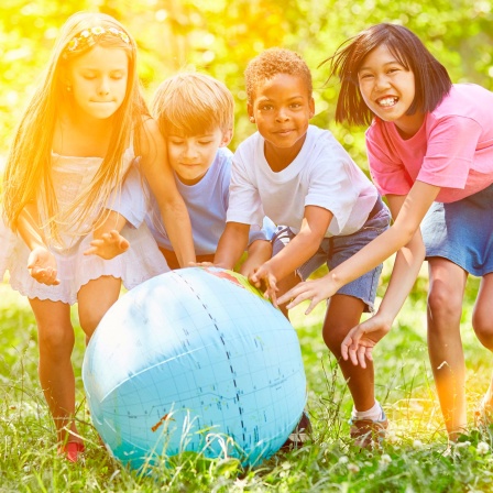 Vier Kinder unterschiedlicher Herkunft spielen mit einer Weltkugel