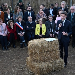 Der französische Premierminister Gabriel Attal spricht während eines Besuchs auf einem Bauernhof in Südwestfrankreich. Der mit einem Anzug bekleidete Politiker steht vor einem Strohballen, hintern ihm sitzen Personen auf Stühlen. 