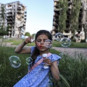 Kyiv, 5-jähriges Mädchen pustet Seifenblasen vor zerbometen Häusern in die Luft © picture alliance / AA / Metin Aktas