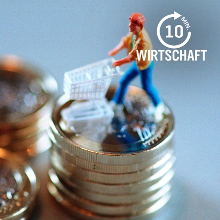 Eine Spielfigur zeigt einen Mann mit leerem Einkaufswagen auf einem Stapel von 1-Euro-Münzen.